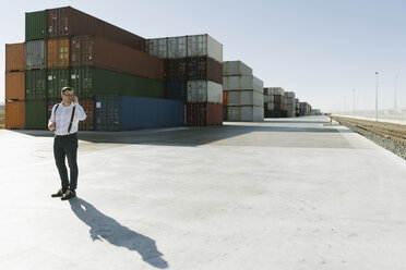Manager, der vor Frachtcontainern auf einem Industriegelände mit seinem Handy telefoniert - AHSF00218