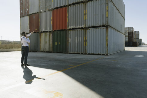Manager, der vor Frachtcontainern auf einem Industriegelände mit seinem Handy telefoniert - AHSF00219