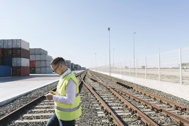 Man on railway tracks in front of cargo containers using cell phone - AHSF00221