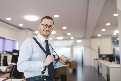 Porträt eines selbstbewussten Geschäftsmannes, der mit Hosenträgern im Büro posiert - AHSF00238