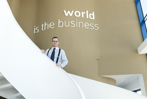 Porträt eines selbstbewussten Geschäftsmannes auf einer Treppe in einem modernen Büro - AHSF00244