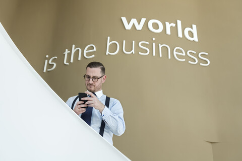 Geschäftsmann benutzt Mobiltelefon auf einer Treppe in einem modernen Büro, lizenzfreies Stockfoto