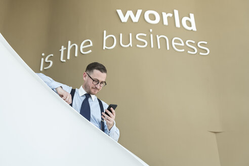 Geschäftsmann benutzt Mobiltelefon auf einer Treppe in einem modernen Büro - AHSF00248
