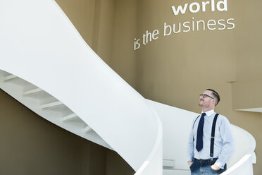 Confident businessman looking up stairs in modern office - AHSF00252