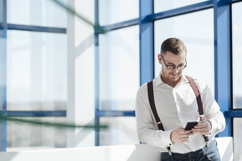 Geschäftsmann mit Handy am Fenster in einem modernen Büro, lizenzfreies Stockfoto