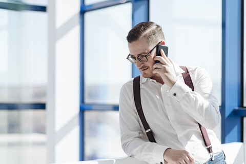 Geschäftsmann im Gespräch mit Handy am Fenster in einem modernen Büro, lizenzfreies Stockfoto