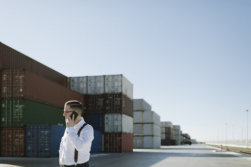 Manager, der vor Frachtcontainern auf einem Industriegelände mit seinem Handy telefoniert - AHSF00275