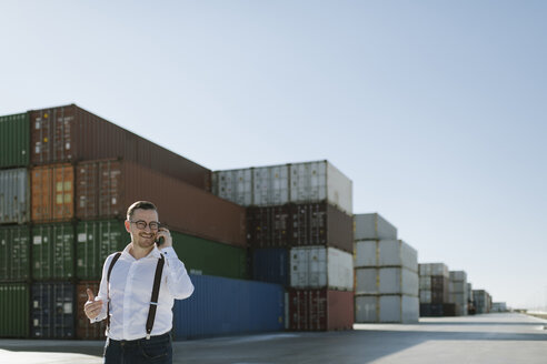Manager, der vor Frachtcontainern auf einem Industriegelände mit seinem Handy telefoniert - AHSF00276