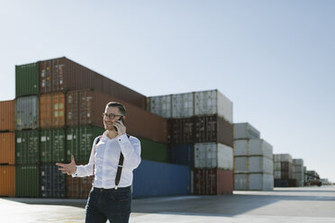 Manager, der vor Frachtcontainern auf einem Industriegelände mit seinem Handy telefoniert - AHSF00277