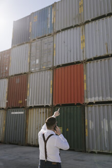 Rückansicht eines Managers, der vor einem Frachtcontainer auf einem Industriegelände mit einem Handy telefoniert - AHSF00278