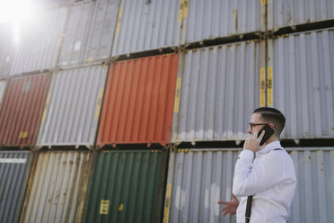 Manager, der vor Frachtcontainern auf einem Industriegelände mit seinem Handy telefoniert - AHSF00279