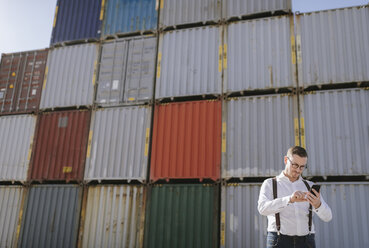 Manager vor Frachtcontainern auf einem Industriegelände mit Mobiltelefon - AHSF00280