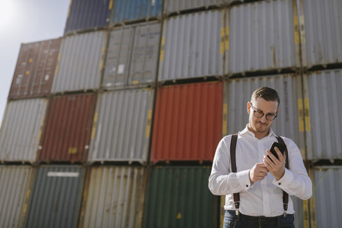 Manager vor Frachtcontainern auf einem Industriegelände mit Mobiltelefon - AHSF00281