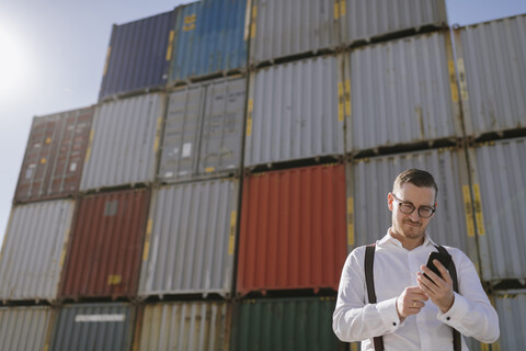 Manager vor Frachtcontainern auf einem Industriegelände mit Mobiltelefon, lizenzfreies Stockfoto