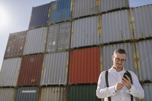 Manager vor Frachtcontainern auf einem Industriegelände mit Mobiltelefon - AHSF00282