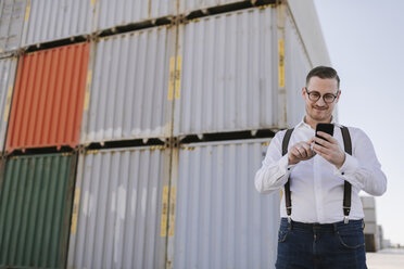 Manager vor Frachtcontainern auf einem Industriegelände mit Mobiltelefon - AHSF00283