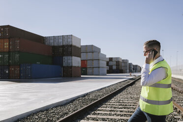Mann auf Bahngleisen vor Frachtcontainern, der mit seinem Handy telefoniert - AHSF00285