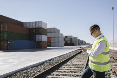 Mann auf Bahngleisen vor Frachtcontainern mit Mobiltelefon, lizenzfreies Stockfoto