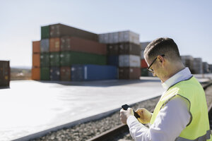 Mann auf Bahngleisen vor Frachtcontainern mit Mobiltelefon - AHSF00287