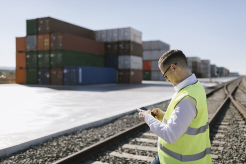 Mann auf Bahngleisen vor Frachtcontainern mit Mobiltelefon - AHSF00288