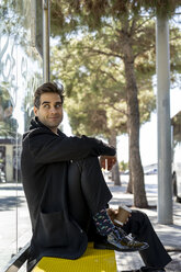 Spanien, Barcelona, lächelnder Mann sitzt auf einer Bank am Bahnhof - AFVF02876