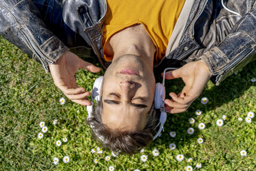 Man lying on flower meadow with headphones - AFVF02889