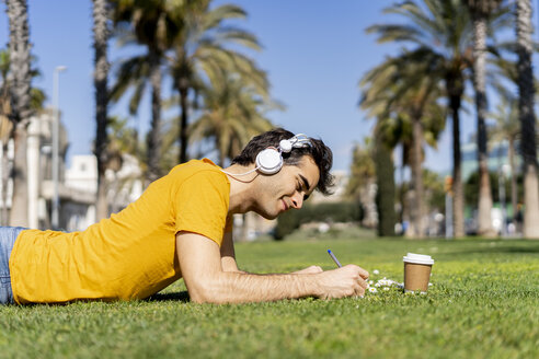 Spanien, Barcelona, Mann liegt mit Kopfhörern und Notebook auf einer Wiese in der Stadt - AFVF02890