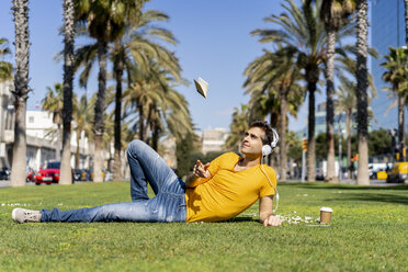 Spanien, Barcelona, Mann liegt mit Kopfhörern auf einer Wiese in der Stadt und übergibt sich mit einem Notebook - AFVF02893