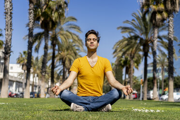 Spain, Barcelona, man practicing yoga on lawn in the city - AFVF02895