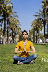 Spain, Barcelona, man practicing yoga on lawn in the city - AFVF02896