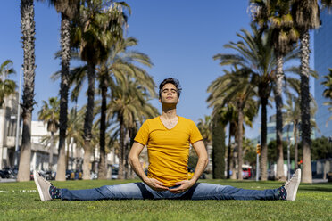 Spain, Barcelona, man practicing yoga on lawn in the city - AFVF02899