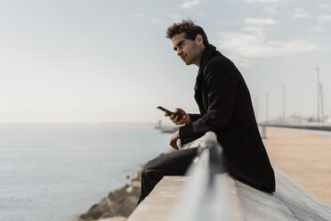 Businessman sitting on quay wall with cell phone - AFVF02902