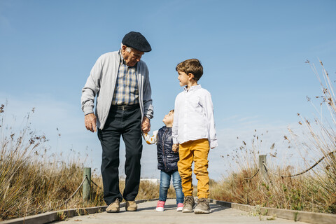 Grandfather strolling with his grandchildren hand in hand on boardwalk stock photo