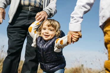 Porträt eines glücklichen kleinen Mädchens, das mit Großvater und Bruder Hand in Hand in der Natur spazieren geht - JRFF03180
