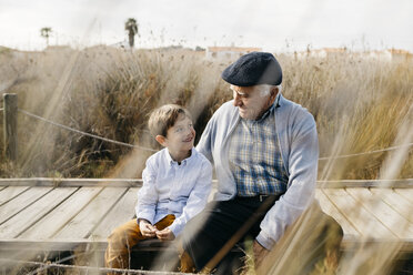 Grandfather sitting with his grandson on boardwalk talking - JRFF03182