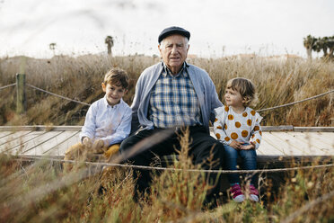 Portrait of grandfather sitting with his grandchildren side by side on boardwalk - JRFF03183