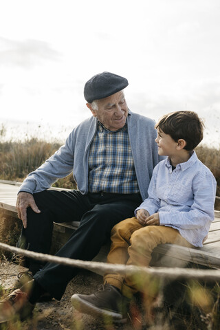 Grandfather sitting with his grandson on boardwalk looking at each other stock photo