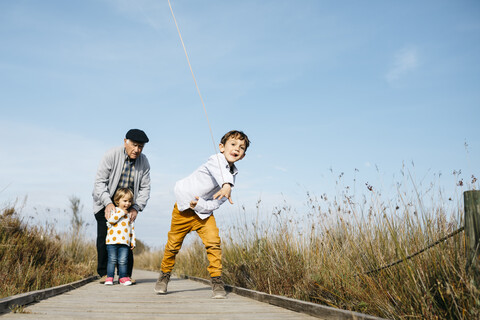 Boy on boardwalk throwing stick while his grandfather and his little sister watching him from the background stock photo