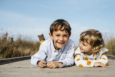 Porträt eines Jungen und seiner kleinen Schwester, die nebeneinander auf der Strandpromenade liegen und Spaß haben - JRFF03190