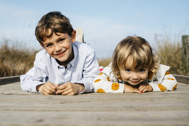 Porträt eines lächelnden Jungen und seiner kleinen Schwester, die Seite an Seite auf der Promenade liegen - JRFF03191