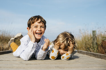 Porträt eines lachenden Jungen und seiner kleinen Schwester, die Seite an Seite auf der Promenade liegen - JRFF03193