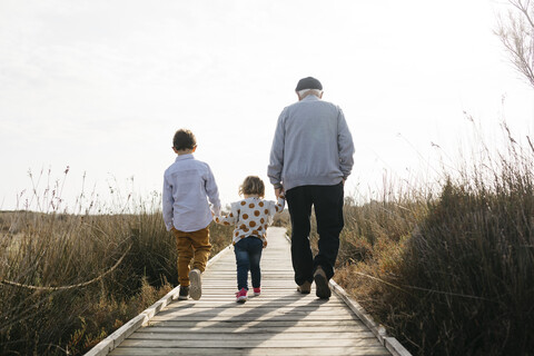 Rückenansicht von Großvater und Enkelkindern, die Hand in Hand über die Promenade schlendern, lizenzfreies Stockfoto