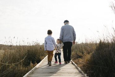 Back view of grandfather and grandchildren strolling hand in hand on boardwalk - JRFF03195