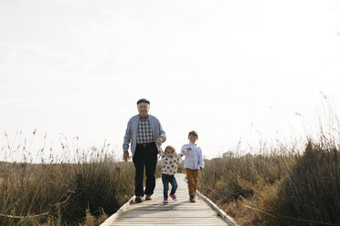 Großvater und Enkelkinder schlendern Hand in Hand über die Strandpromenade - JRFF03196