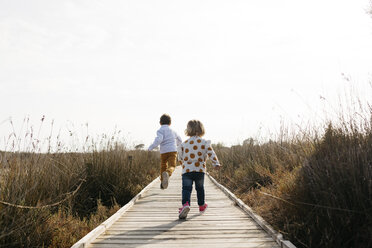 Back view of two little children running on boardwalk - JRFF03197