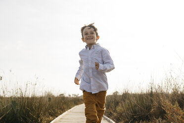 Porträt eines glücklichen kleinen Jungen, der auf der Strandpromenade läuft - JRFF03200