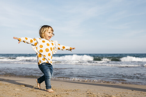 Glückliches kleines Mädchen läuft barfuß am Strand, lizenzfreies Stockfoto