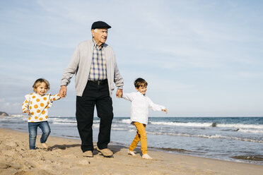 Grandfather strolling with his grandchildren hand in hand on the beach - JRFF03207