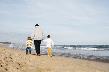 Back view of grandfather strolling with his grandchildren hand in hand on the beach - JRFF03208