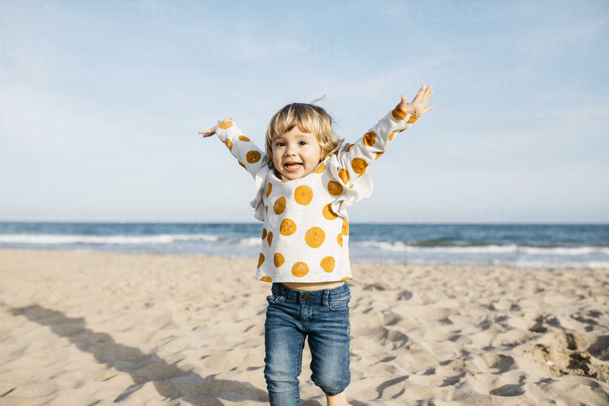 Portrait of smiling little girl running on beach stock photo - OFFSET